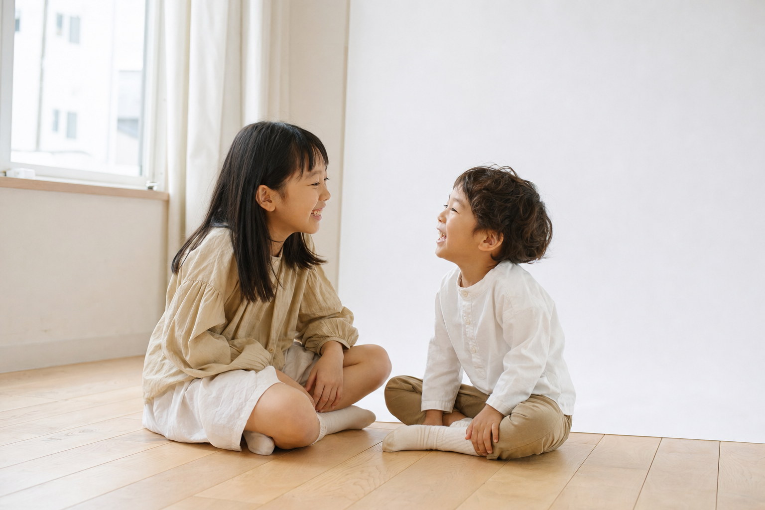 木の床で向かい合って笑う姉と弟(掲載イメージ)