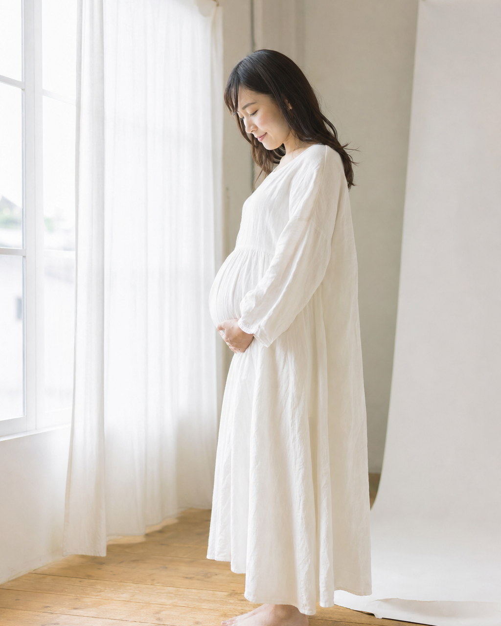 窓辺でおなかに手を添えて立つ女性(掲載イメージ)