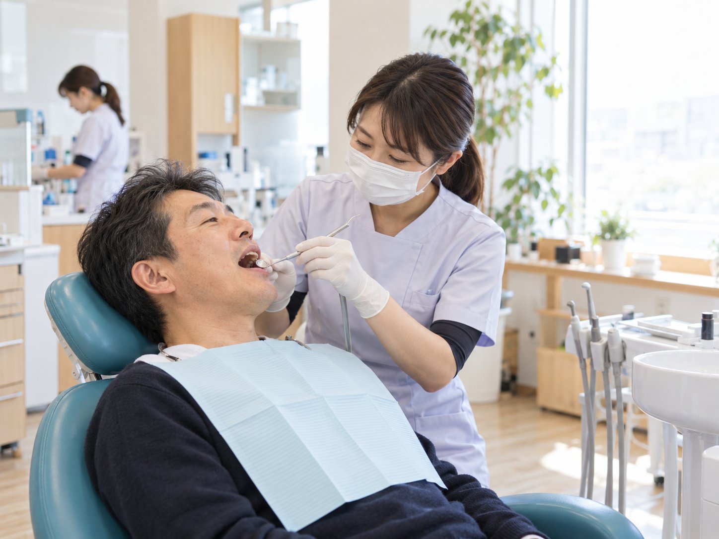 診療台に横になった男性の歯を、マスクをした歯科衛生士がクリーニングしている様子